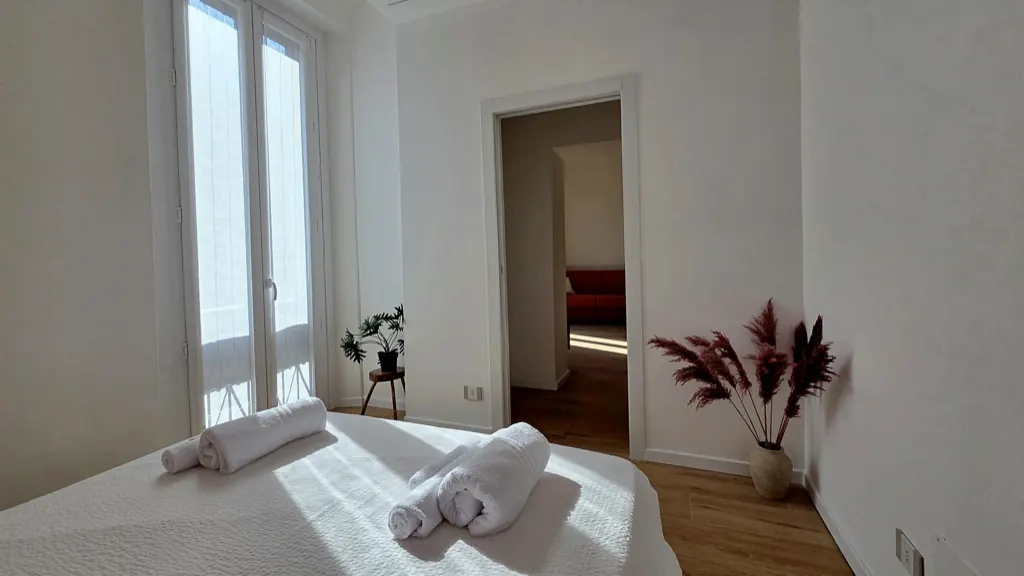 Camera luminosa con portafinestra, piante e asciugamani pronti sul letto